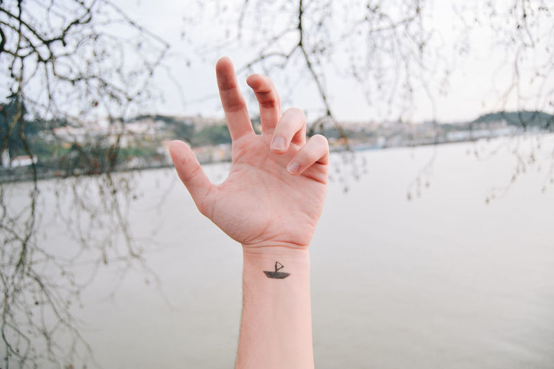 Close-up of cropped hand showing tattoo against river