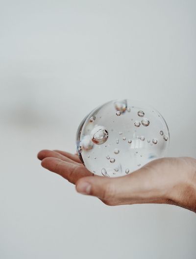 Cropped hand holding bubble against white background