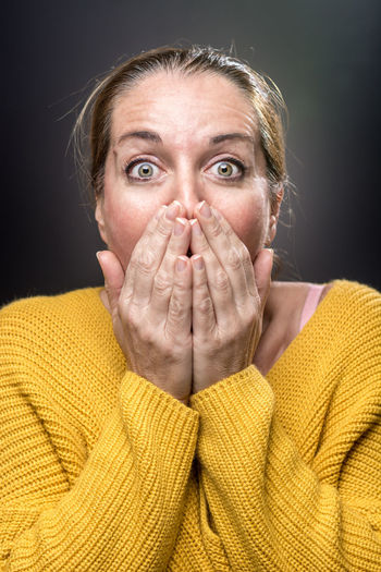 Portrait of woman covering mouth against black background