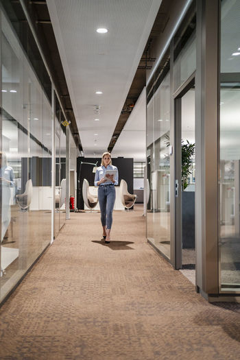 Businesswoman with tablet pc walking in office corridor