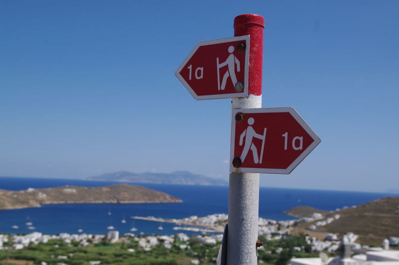 Close-up of road sign by sea against clear blue sky