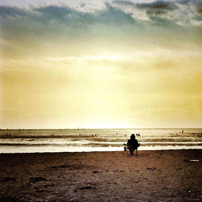 Lone person sitting on beach overlooking sea