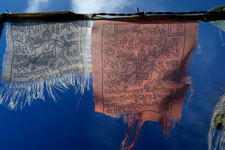 Low angle view of prayer flags hanging against blue sky on sunny day