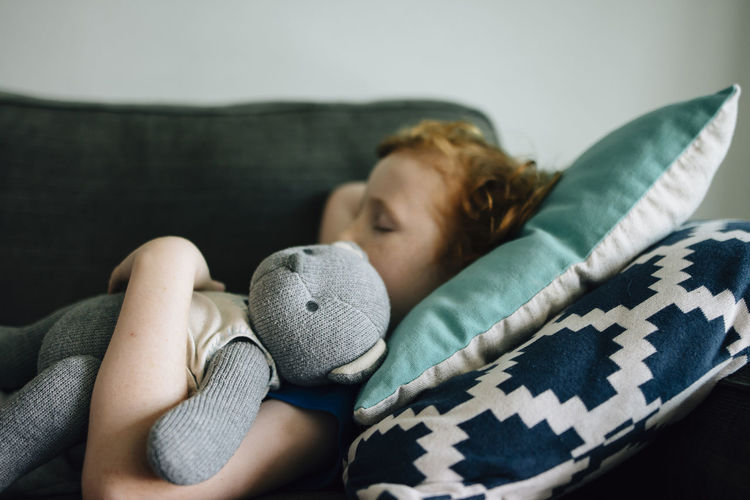 Side view of boy sleeping with teddy bear on couch at home