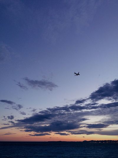 Silhouette airplane flying over sea against blue sky