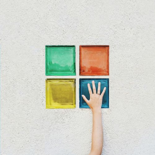 Close-up of human hand against multi colored wall