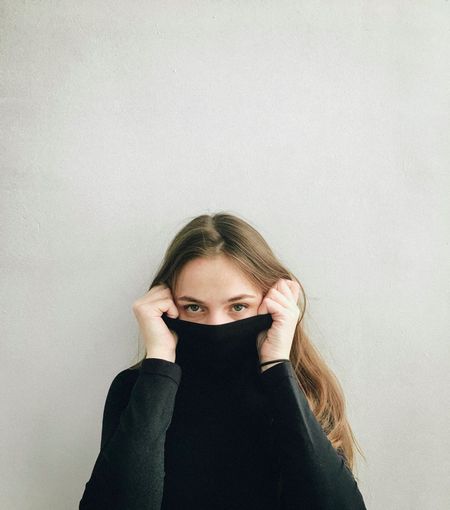 Portrait of young woman covering face against wall