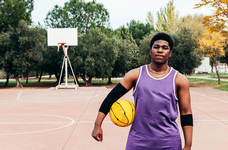 Black african-american boy playing basketball with a yellow ball on a court. 