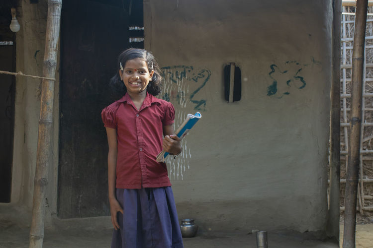 Portrait of smiling girl standing against door holding book