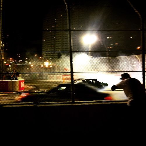 Rear view of man watching racing car through chainlink fence at night