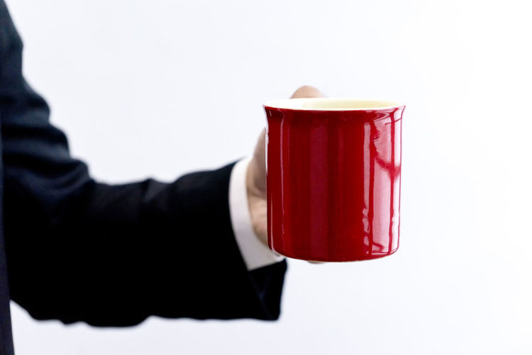 Close-up of hand holding red cup over white background