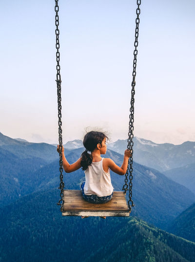 Girl sitting on swing at playground against sky