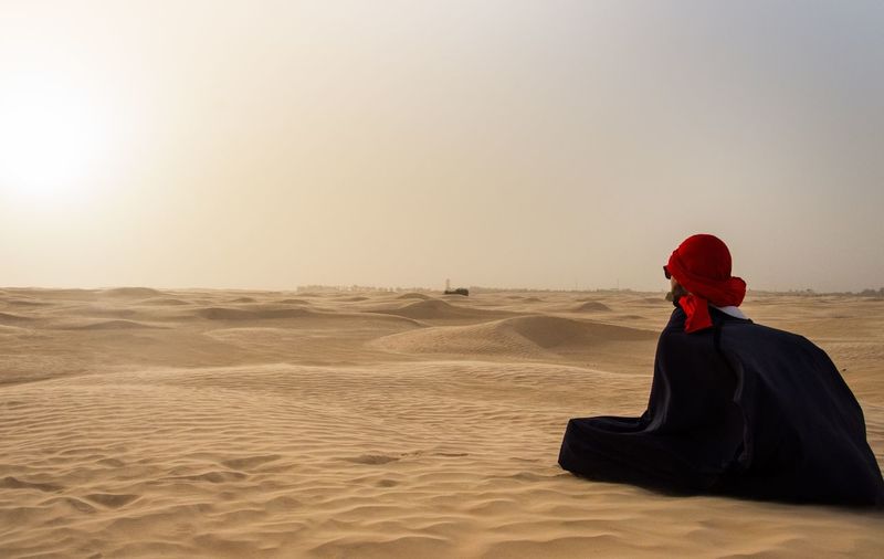 Woman relaxing on desert against sky