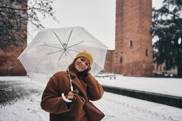 Portrait of smiling young woman with umbrella standing against wall