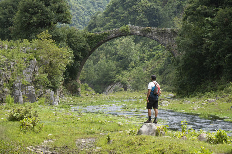 One man standing on a rock under an ancient bridge on a river