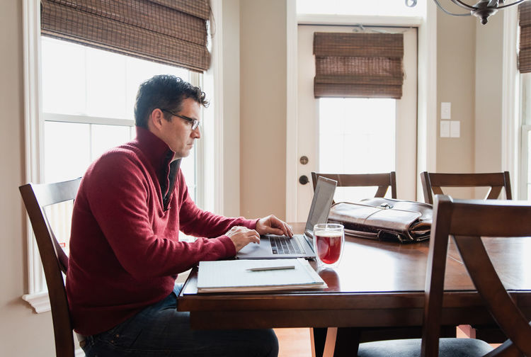 Man in glasses working from home using a computer at a dining table.