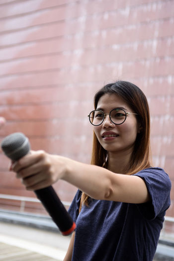 Female journalist with microphone standing against building