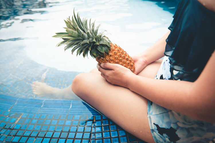 Midsection of woman holding pineapple sitting by pool