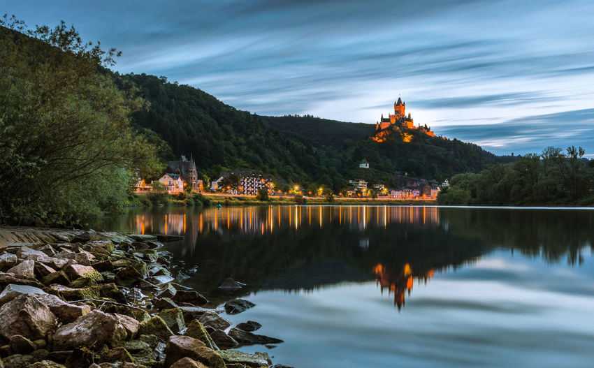 Scenic view of cochem imperial castle on mountain reflecting in river at dusk