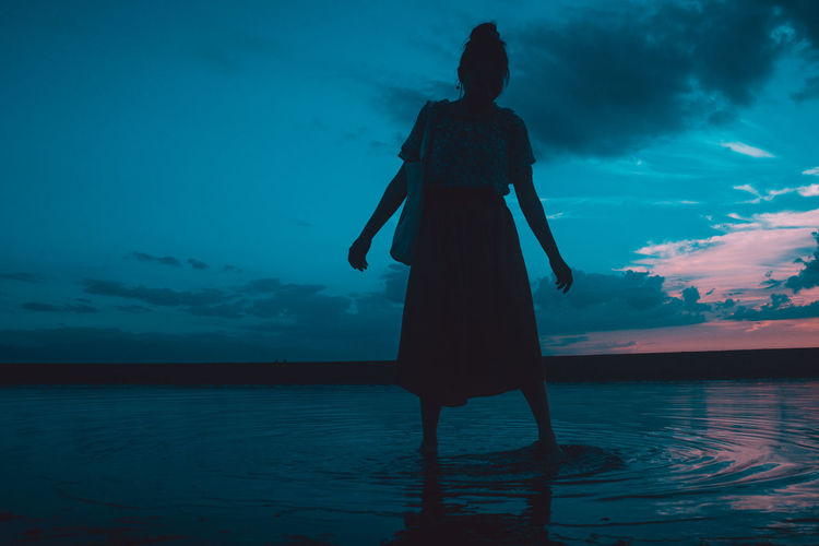Rear view of silhouette woman standing by sea against sky