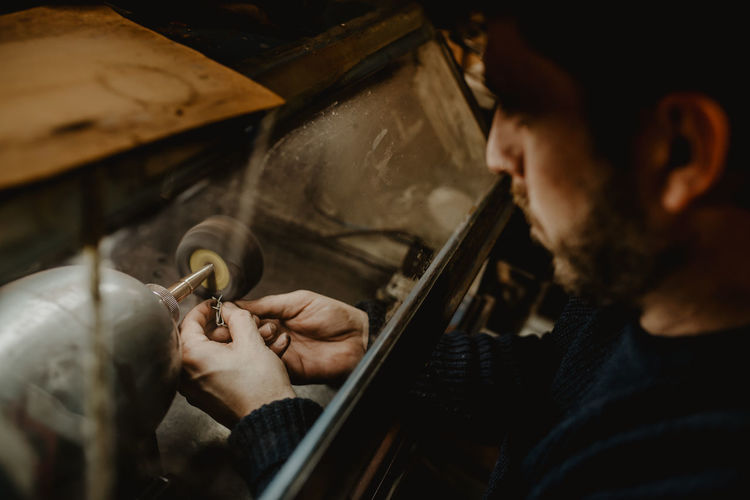 Hands of anonymous male goldsmith using manual tool to shape metal ring in workshop