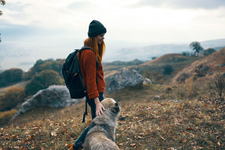 Rear view of woman with dog on mountain against sky