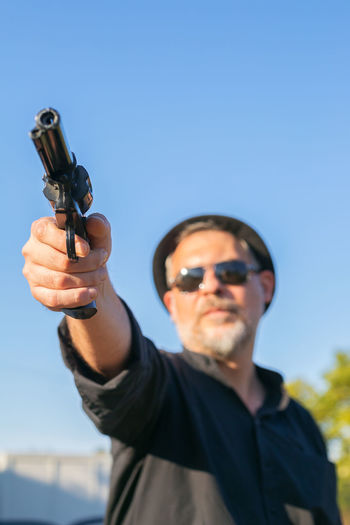 Low angle view of man holding gun against sky