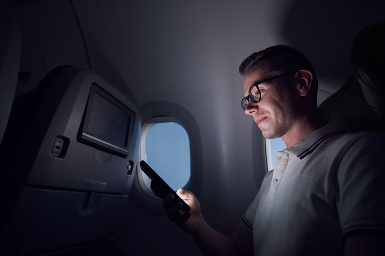 Man traveling by airplane. passenger using phone during night flight.