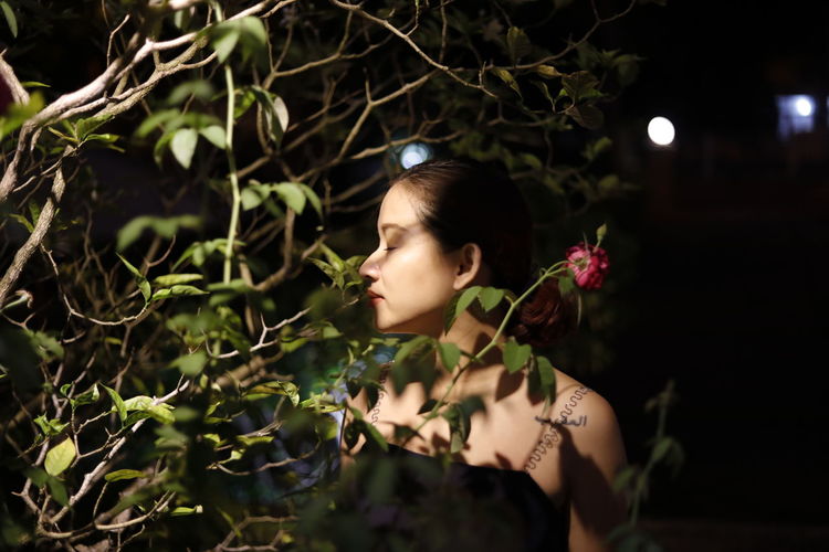 Close-up of beautiful woman with flowers on tree at night