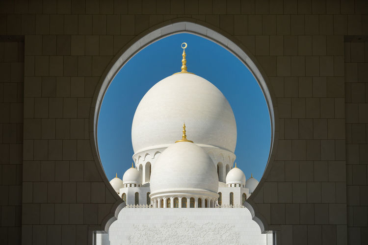 Domes of sheikh zayed mosque seen through arch