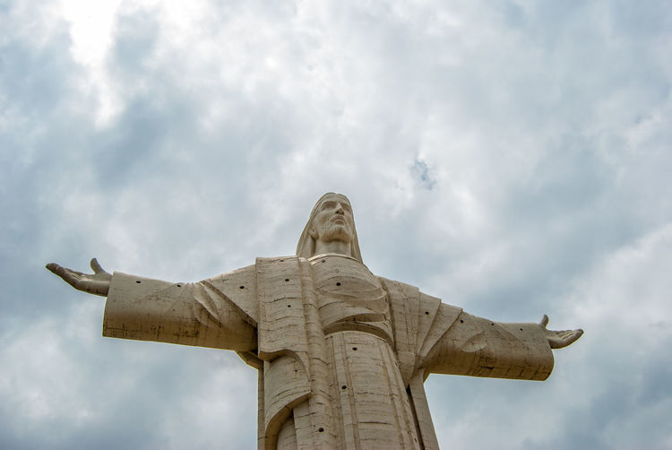 Low angle view of jesus statue against cloudy sky