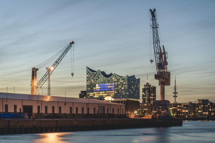 Germany, hamburg, harbor cranes at dusk with elbphilharmonie in background