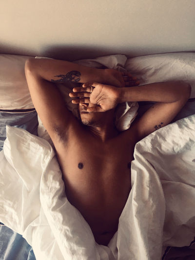 Midsection of shirtless man lying in bed