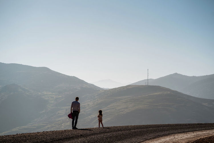 Rear view of father and daughter looking at mountain against clear sky