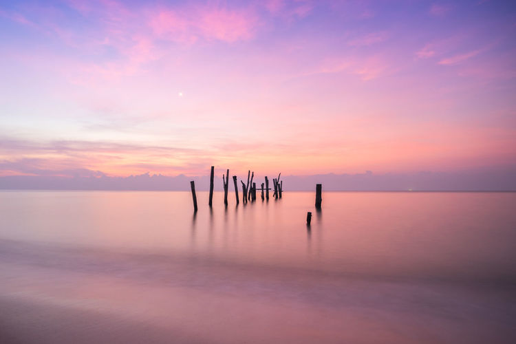Silhouette wooden posts in sea against sky during sunset