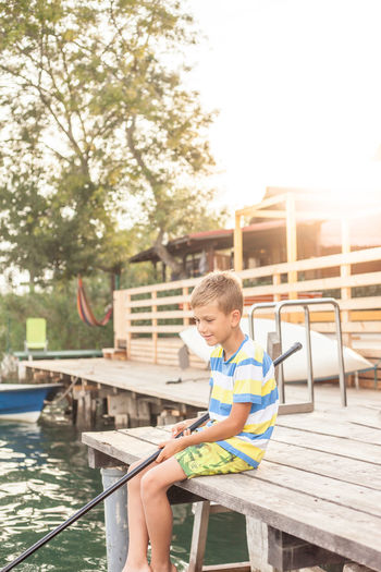 Boy fishing in lake while sitting on pier