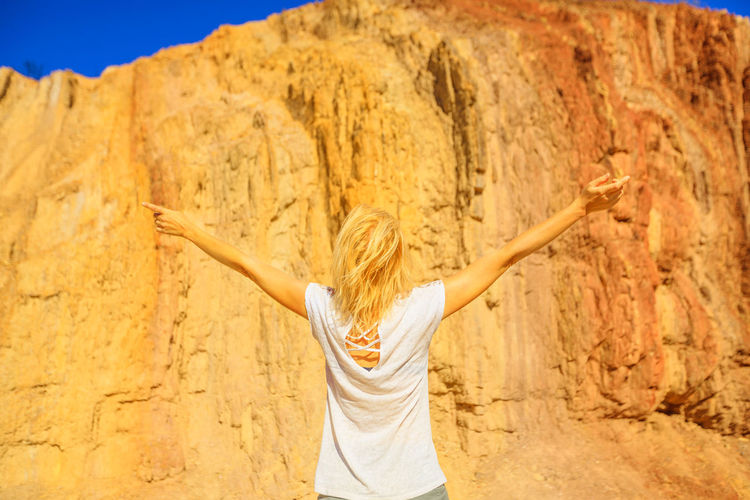 Rear view of woman with arms raised standing against wall