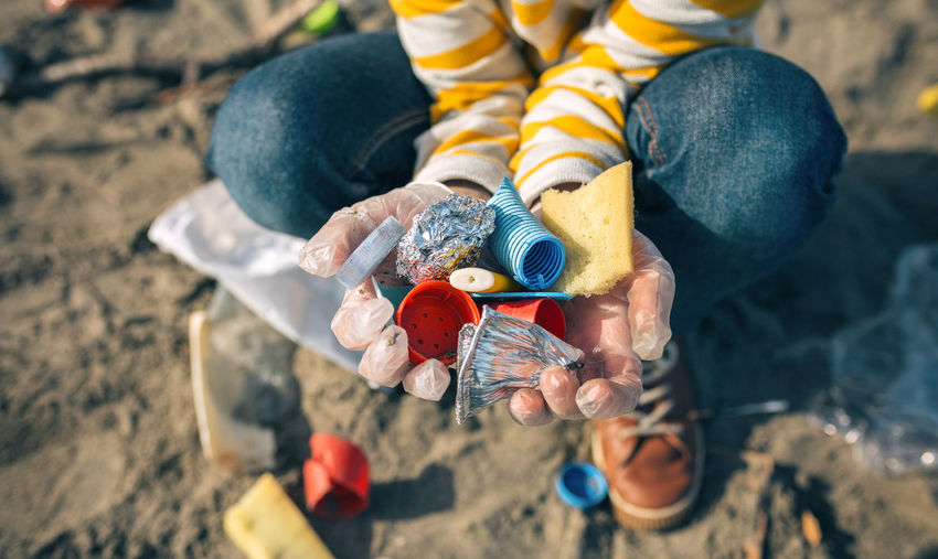 Close-up high angle view of boy holding garbage while crouching at beach