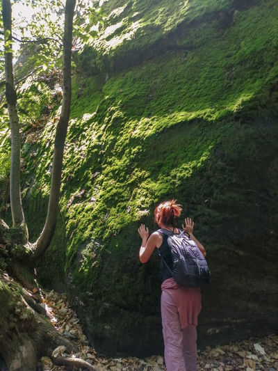 Rear view of woman standing in forest, touching and smelling moss
