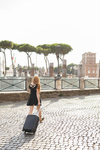 Female traveler with suitcase walking on city square