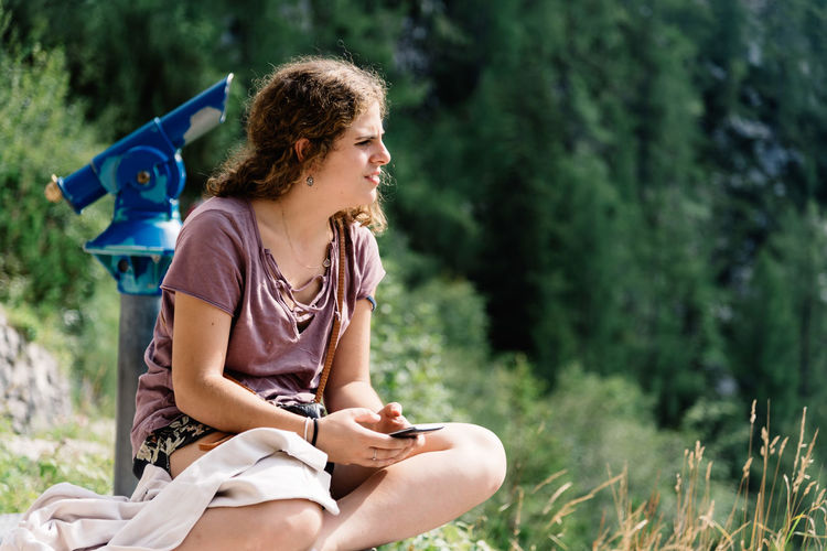 Young woman using mobile phone while sitting against tree