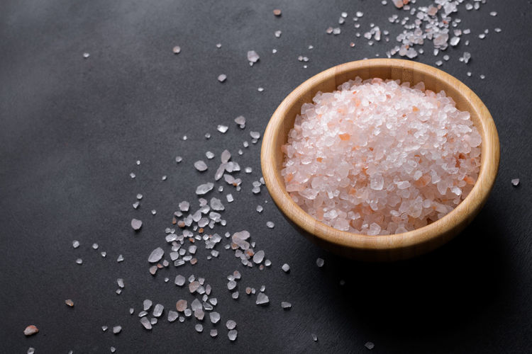 Pink himalayan salt in a wooden bowl with scattered salt on a black background