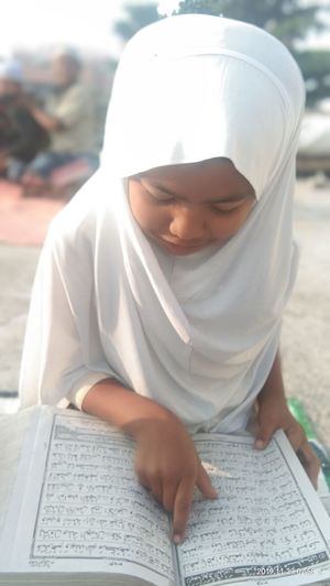 Girl reading koran while sitting outdoors