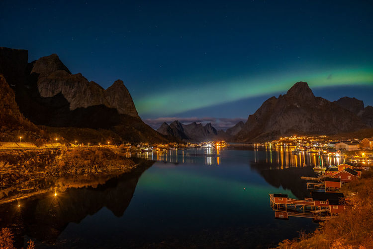 Illuminated lake by mountains against sky at night