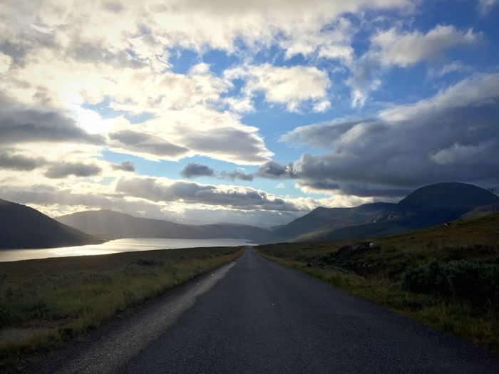 Empty road leading towards mountains against cloudy sky