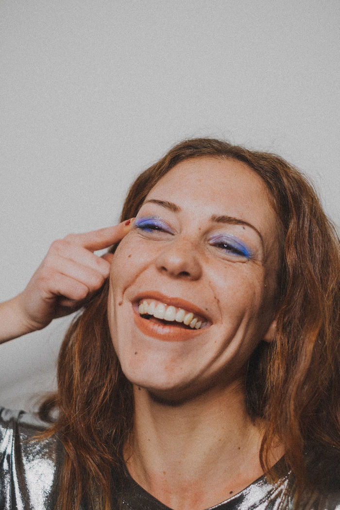 Smiling young woman with eye make-up against wall