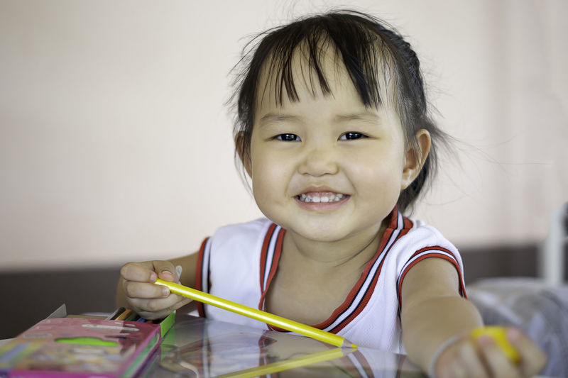 Portrait of cute smiling girl with colored pencil on table