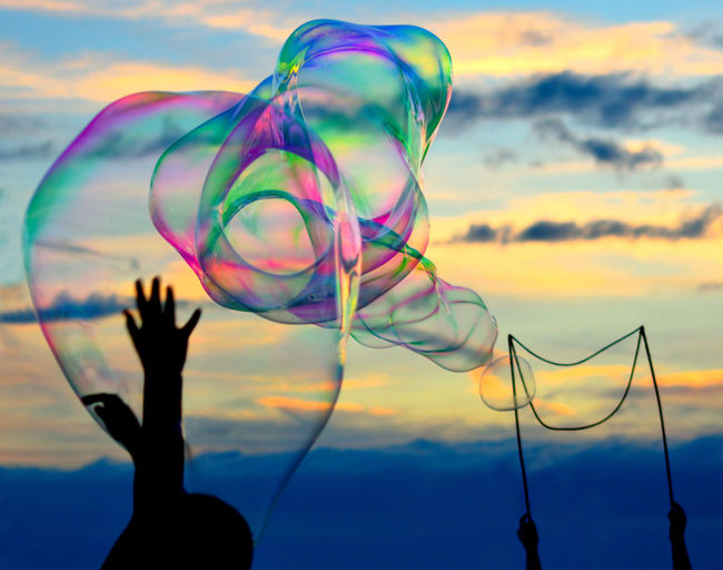 Silhouette person touching bubbles against sky during sunset