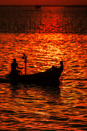 Silhouette man in boat against sky during sunset