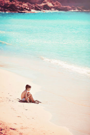Teenage boy sitting at beach during sunny day